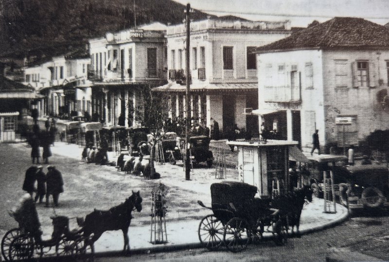 Πλατεία Άργους. «Πιάτσα αγοραίων». Ιππήλατες άμαξες και οκτώ ταξί περιμένουν τους πελάτες.  Αρχές της Δεκαετίας του 1930.