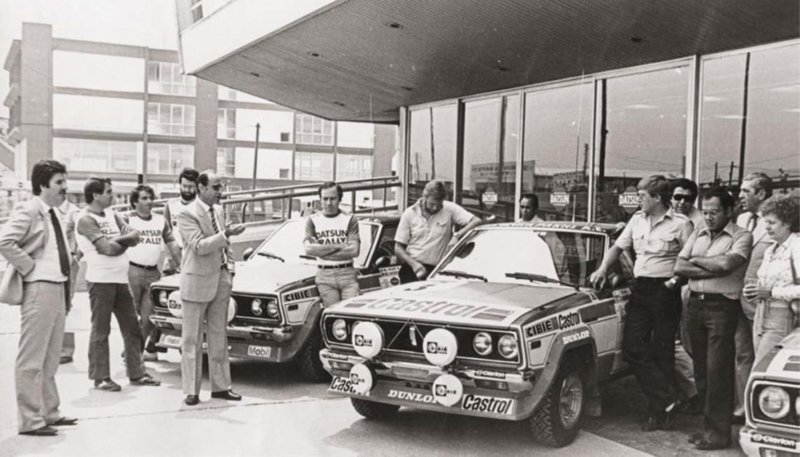 Οι οδηγοί και συνοδηγοί της Nissan στο 29ο Ράλλυ Ακρόπολις, δίπλα στα Datsun HA10, μπροστά από τις εγκασταστάσεις της Λεωφ. Αθηνών 169. Διακρίνεται, ο Βασίλης Θεοχαράκης και δεξιά του ο Γ. Μοσχούς. Δίπλα του, ο Τ. Σάλονεν και Σ. Μέτα.