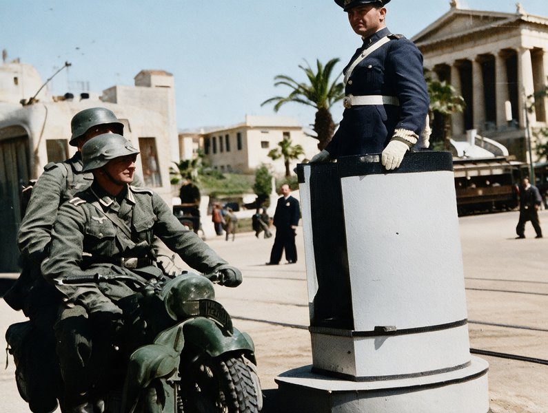 Μπροστά από την Εθνική Βιβλιοθήκη, στην οδό Πανεπιστημίου, δύο Γερμανοί με μοτοσυκλέτες περνούν μπροστά από τροχονόμο που κοιτά αγέροχος.  «Τις πόλεις τις φτιάχνουμε μέσω της αστυνομίας», έγραφε ήδη τον 17ο αιώνα ο Γάλλος νομικός Jean Domat...